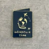 Close-up of a navy blue enamel pin with a globe and airplane design, and the text "adventure time".