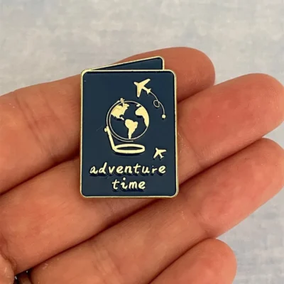 Another angle of the navy blue enamel pin with "adventure time" text, held in a person's hand.