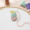 Small embroidered tea cup with a needle and thread, featuring an enamel needle minder beside it.