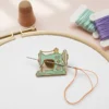 A sewing machine with colorful embroidery thread and an enamel needle minder on a wooden table.
