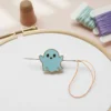 Blue ghost enamel needle minder attached to a needle and thread, showcasing a whimsical sewing accessory.
