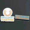 세련된 디자인에 단합과 협업을 상징하는 'Brilliant Together'라는 문구가 새겨진 핀과 배지입니다.
