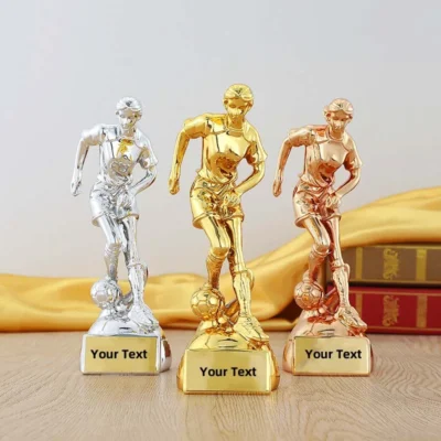 Three gold and silver soccer trophies displayed on a table, showcasing their gleaming surfaces and intricate designs.