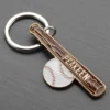 Un portachiavi con mazza da baseball e palla appoggiato su una superficie grigia, che mette in mostra un accessorio giocoso a tema sportivo.