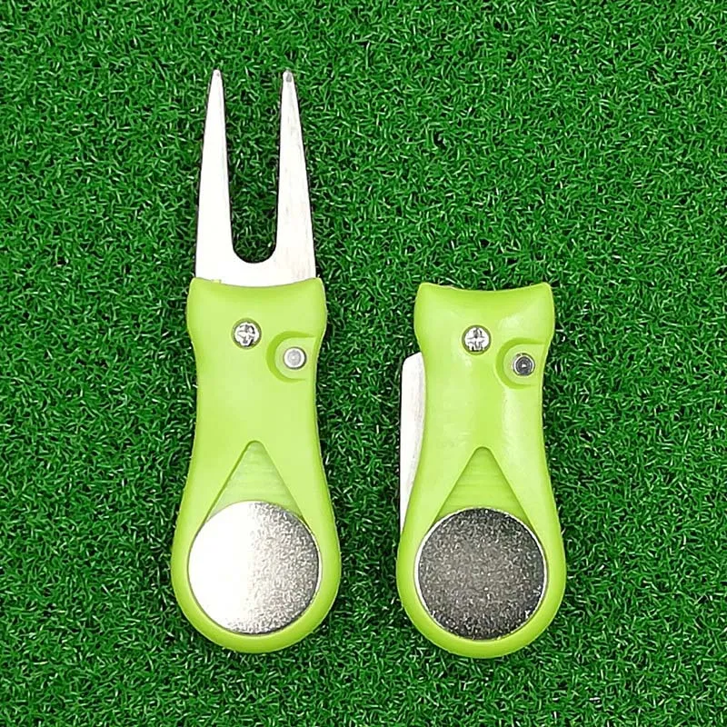 Two green golf divot tools with plastic handles resting on a patch of grass.