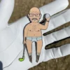 A golf divot tool pin featuring a naked man humorously holding a golf ball.