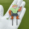 A red panda in a green shirt holds a golf club and a golf divot tool, ready for a playful game on the course.