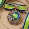 A pickleball medal with a ribbon rests atop a wooden board, showcasing achievement in the sport of pickleball.