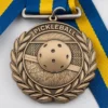 A pickleball medal with a ribbon rests atop a wooden board, showcasing achievement in the sport of pickleball.