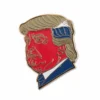 Eine Anstecknadel mit einem Bild von Donald Trump, das seine ikonische Frisur und seinen Ausdruck zeigt.
