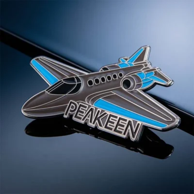 An airplane-shaped pin displaying the word "peaken" prominently.