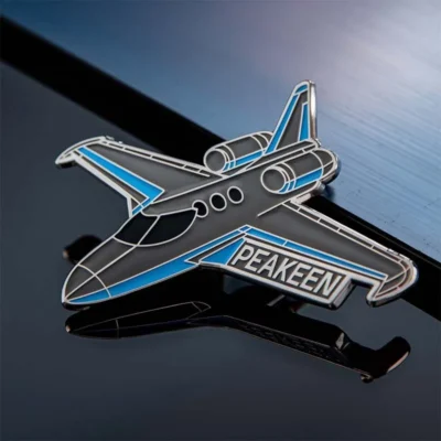 An airplane-shaped pin displaying the word "peaken" prominently.