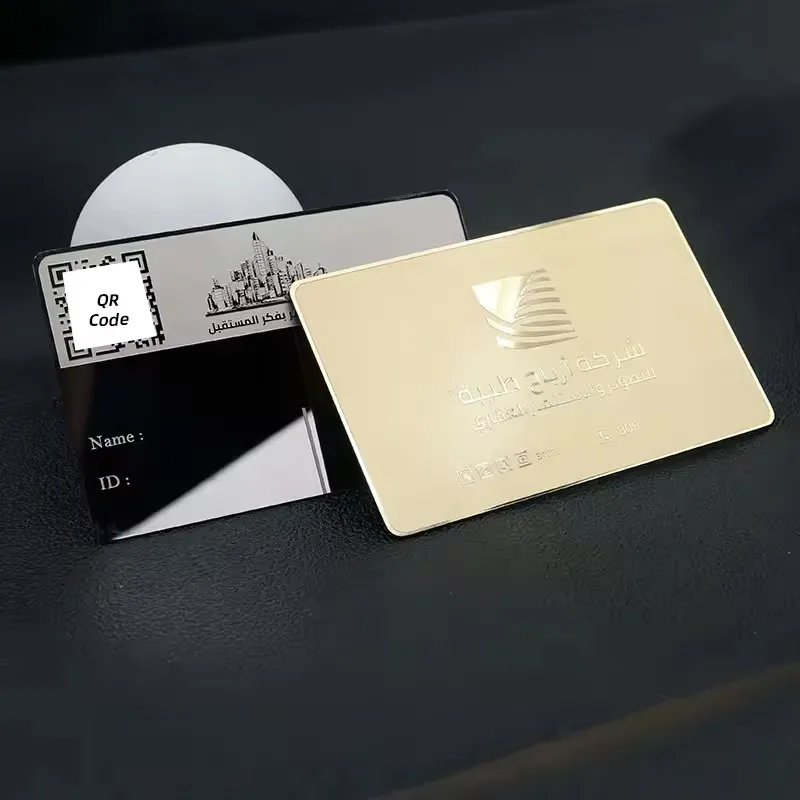 Two metal business cards displayed on a black surface. One card is gold with Arabic text and a logo, while the other is black and silver with a QR code, space for a name, and ID. Keywords: metal business card.