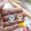 Une personne présentant des boucles d'oreilles en émail souple personnalisées, ornées d'un chat enjoué.