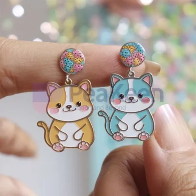 A person showcasing custom soft enamel earrings featuring a playful cat design.