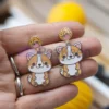 Une personne présentant des boucles d'oreilles en émail souple personnalisées, ornées d'un chat enjoué.