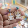Une personne présentant des boucles d'oreilles en émail souple personnalisées, ornées d'un chat enjoué.