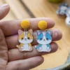 Une personne présentant des boucles d'oreilles en émail souple personnalisées, ornées d'un chat enjoué.