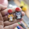 Une personne présentant des boucles d'oreilles en émail souple personnalisées, ornées d'un chat enjoué.