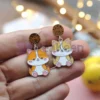 Une personne présentant des boucles d'oreilles en émail souple personnalisées, ornées d'un chat enjoué.