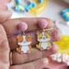 Une personne présentant des boucles d'oreilles en émail souple personnalisées, ornées d'un chat enjoué.