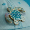 Un chapeau vert orné d'une épingle à tortue personnalisée, un accessoire unique et ludique.