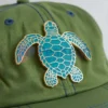 Un chapeau vert orné d'une épingle à tortue personnalisée, un accessoire unique et ludique.
