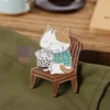 Un gatto appollaiato su una sedia accanto a una tazza di tè, con spille boba personalizzate sullo sfondo.