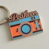 Брелок для фотоаппарата с изображением слова "peakeen" в ярких оранжевых и синих цветах.