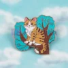 Spilla smaltata con un gatto giocherellone appollaiato su un albero, che sfoggia un design affascinante e stravagante.