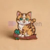 Una simpatica spilla smaltata a forma di gatto su uno sfondo marrone caldo, che mette in mostra il suo design affascinante e i suoi colori vivaci.
