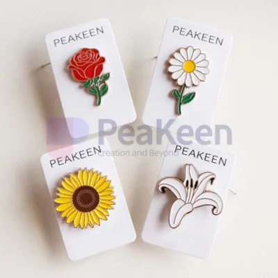 An image showcasing four beautifully crafted soft enamel flower pins: a vibrant red rose, a delicate white daisy with a yellow center, a bright yellow sunflower with a rich brown center, and an elegant white lily. Each pin is mounted on its own sleek paper card, with the brand name 'PeaKeen' prominently printed at the top. The combination of vivid colors and glossy enamel finish highlights the intricate details of each flower, while the uniform presentation on branded cards adds a professional and cohesive touch. Perfect for gifting or retail display.