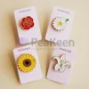 Une image présentant quatre magnifiques épingles à fleurs en émail mou : une rose rouge vibrante, une marguerite blanche délicate avec un centre jaune, un tournesol jaune vif avec un centre marron riche, et un élégant lys blanc. Chaque épingle est montée sur sa propre carte en papier lisse, avec le nom de la marque "PeaKeen" imprimé en évidence dans la partie supérieure. La combinaison de couleurs vives et la finition émaillée brillante mettent en valeur les détails complexes de chaque fleur, tandis que la présentation uniforme sur des cartes de marque ajoute une touche professionnelle et cohérente. Parfait pour les cadeaux ou la vente au détail.
