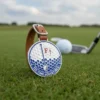 A golf ball and club resting on green grass, with golf bag tags visible in the background.