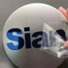 Una persona sostiene una pegatina metálica en la que se lee "sian", con un diseño elegante y moderno.