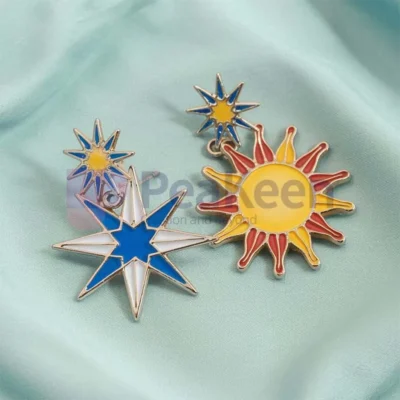 Two enamel pins featuring a sun and moon design on a vibrant blue background, showcasing custom star and sun earrings.