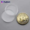 Una moneda física de bitcoin colocada junto a un recipiente de plástico transparente, para resaltar el aspecto tangible de la criptomoneda.