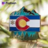 Pin de la bandera de Colorado con montañas y árboles, símbolo de la belleza natural y el orgullo del estado.