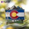 Pin de la bandera de Colorado con montañas y árboles, símbolo de la belleza natural y el orgullo del estado.