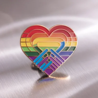 A vibrant rainbow heart pin displayed on a shiny metal surface, symbolizing LGBT pride and inclusivity.