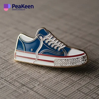 Blue and white sneaker pin featuring the word "peaken," designed for shoe enthusiasts.