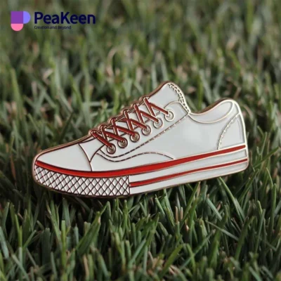 A white and red sneaker pin resting on green grass, showcasing a stylish accessory for shoe enthusiasts.