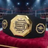 Gold wrestling champion belt with custom text, featuring world class and championship side plates, displayed in a wrestling ring arena
