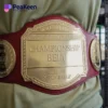 A man showcases a wrestling championship belt, featuring red and gold colors, around his waist.