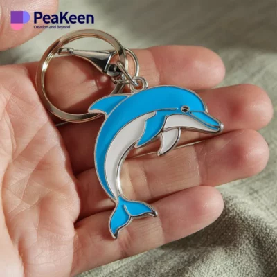 A hand holding a metal dolphin keychain, showcasing its sleek design and vibrant details.