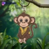 A soft enamel monkey keychain dangles from a tree branch, showcasing its playful design and vibrant colors.