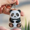 A soft enamel panda bear keychain is held in a person's hand, showcasing its cute design and vibrant colors.