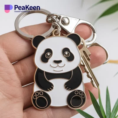 A soft enamel panda bear keychain is held in a person's hand, showcasing its cute design and vibrant colors.