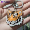 A person holds a soft enamel keychain featuring a detailed tiger face, showcasing vibrant colors and intricate design.