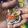 A person holds a soft enamel keychain featuring a detailed tiger face design.